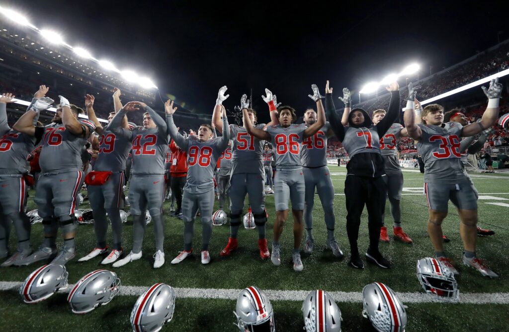 The Ohio State Buckeyes team in Gray and red uniforms celebarting in the endzone post-game facing the fans