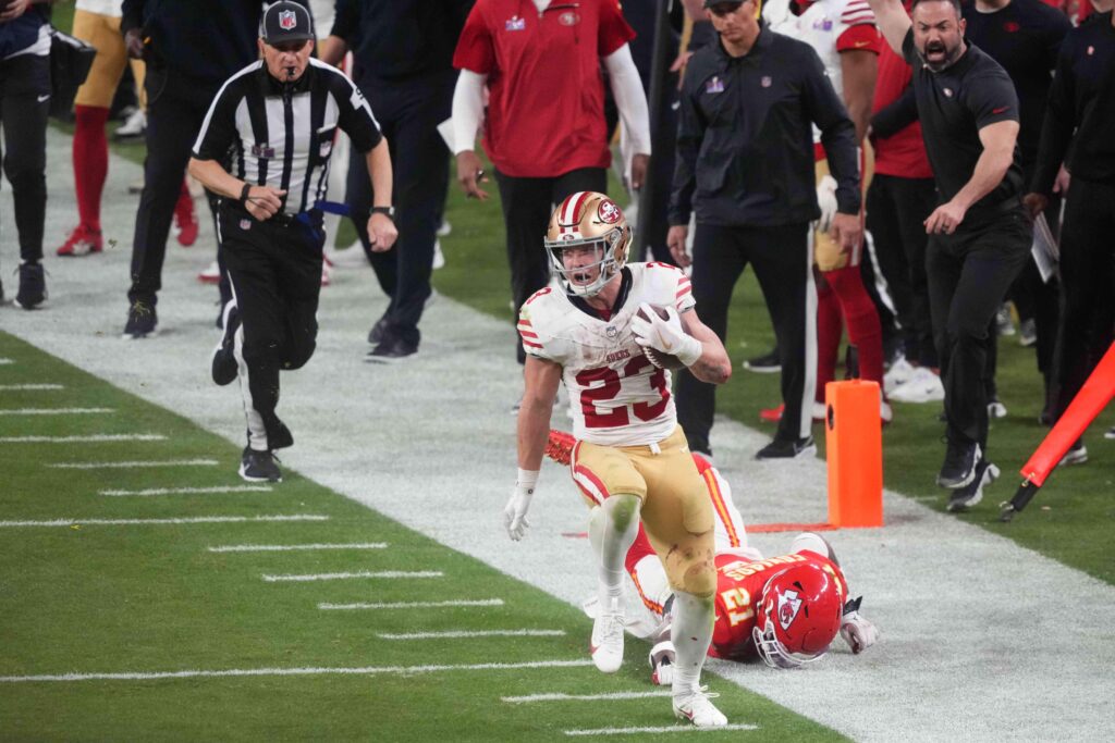 San Francisco 49ers running back (in a white and gold jersey) runs down the sideline evading a Kansas City Chiefs defender (in the red jersey) during Super Bowl LVIII in Las Vegas on Feb. 11, 2024. 